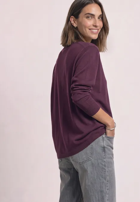 Eenvoudige trui met boothals berry maroon Vrouw in paarse trui en grijze jeans kijkt glimlachend over haar schouder.