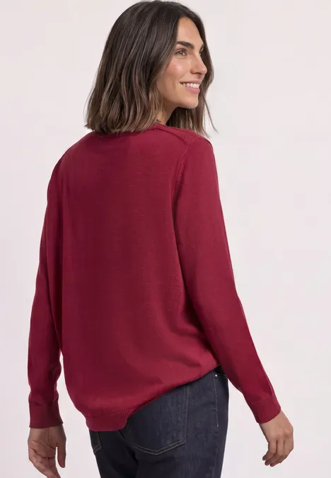 Eenvoudige trui met boothals inferno red Vrouw in bordeauxrode trui en jeans, glimlacht over haar schouder.