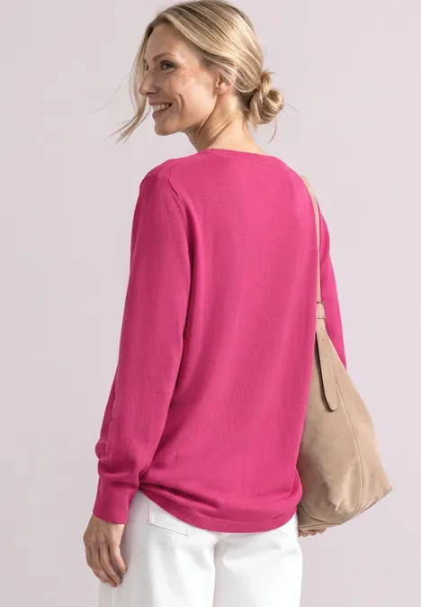 Eenvoudige trui met boothals impact pink Vrouw in profiel draagt roze trui, witte broek en een beige schoudertas.