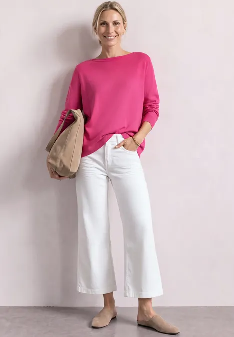 Eenvoudige trui met boothals impact pink Vrouw in roze trui, witte cropped jeans en beige schoenen, glimlachend met papieren tas in hand.