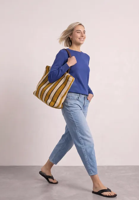 Eenvoudige trui met boothals bold blue Vrouw in blauwe trui en spijkerbroek, met gestreepte tas en zwarte sandalen, wandelt vrolijk.