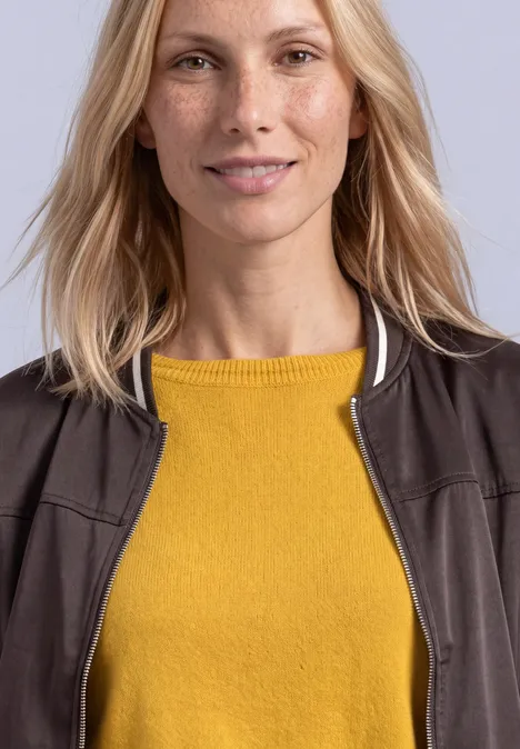 Eenvoudige trui met boothals saffron yellow Eine lächelnde blonde Frau trägt einen gelben Pullover und eine braune Jacke vor hellem Hintergrund.