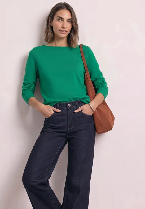 Eenvoudige trui met boothals kelly green Vrouw met een groene trui, donkerblauwe jeans en een bruine schoudertas tegen een lichte achtergrond.