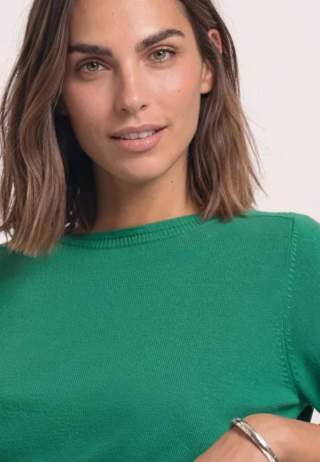 Eenvoudige trui met boothals kelly green Een vrouw met halflang bruin haar draagt een groene trui en glimlacht zachtjes.
