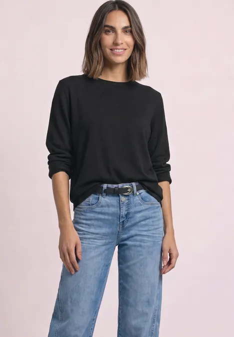 Trui met ronde hals en omgeslagen randen Black Een vrouw in een zwarte trui en blauwe jeans poseert voor een lichte achtergrond.