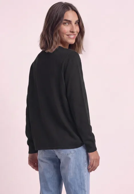 Trui met ronde hals en omgeslagen randen Black Een vrouw in een zwarte trui en blauwe jeans kijkt over haar schouder.