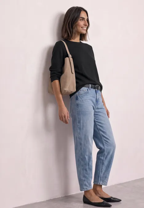 Trui met ronde hals en omgeslagen randen Black Vrouw leunt tegen muur, draagt zwarte trui, lichtblauwe spijkerbroek, zwarte ballerina’s en een beige tas.