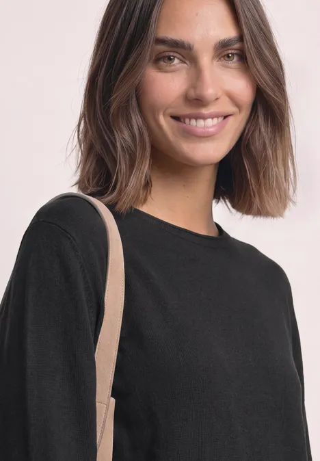 Trui met ronde hals en omgeslagen randen Black Glunderende vrouw in zwart shirt met beige schouderriem tegen een lichte achtergrond.