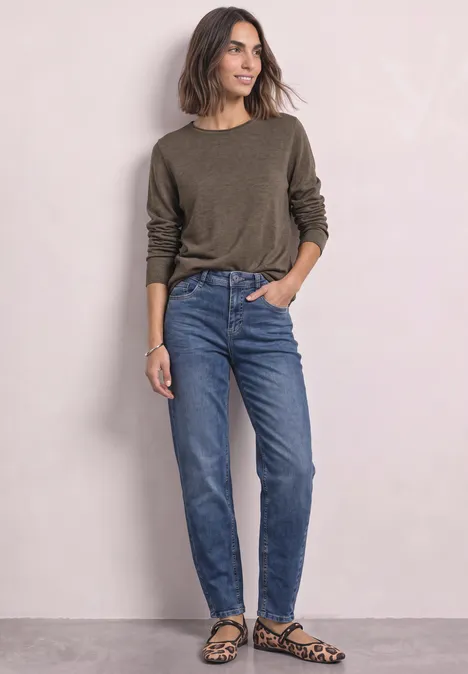Trui met ronde hals en omgeslagen randen nomad brown mel. Vrouw in groene trui, blauwe jeans en luipaardprint ballerina's voor lichte achtergrond.