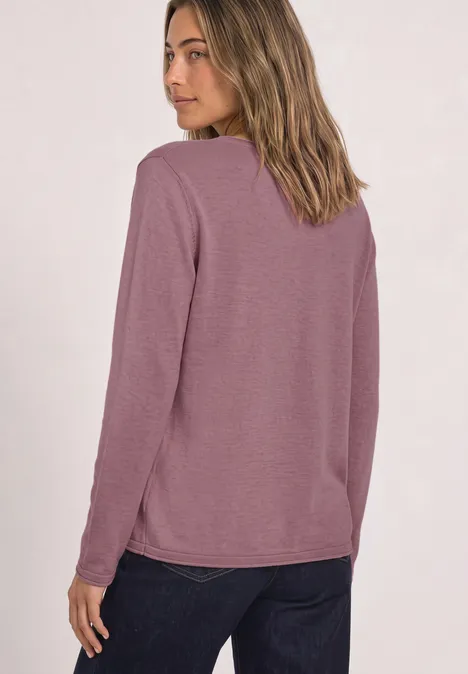 Frau von hinten in mauvefarbenem Langarmshirt und dunkler Jeans, Blick über die Schulter.