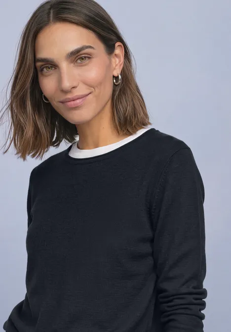 Eine lächelnde Frau mit braunen mittellangen Haaren, trägt schwarzen Pullover und weißen Kragen.