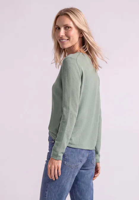 Trui met ronde hals en omgeslagen randen eucalyptus green mel. Zijaanzicht van een vrouw met groene trui en spijkerbroek, glimlachend en over haar schouder kijkend.