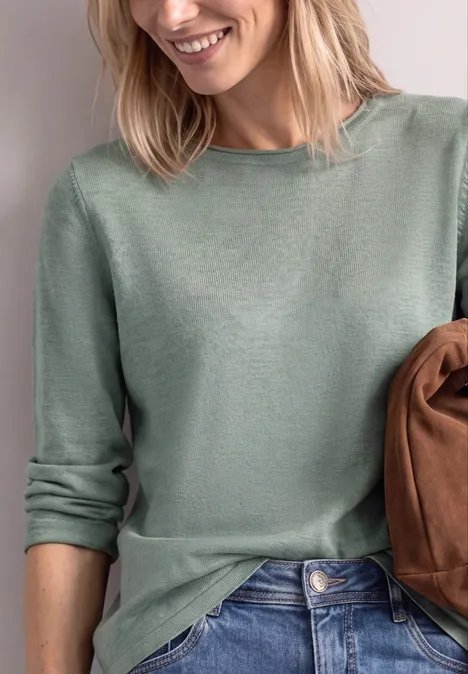 Trui met ronde hals en omgeslagen randen eucalyptus green mel. Vrouw draagt lichtgroene trui en houdt een bruine tas vast.