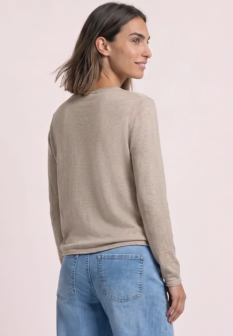 Trui met ronde hals en omgeslagen randen clay sand mel. Vrouw van achteren in een beige trui en blauwe spijkerbroek, kijkt opzij.