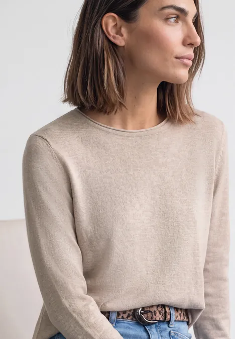 Trui met ronde hals en omgeslagen randen clay sand mel. Vrouw met kort bruin haar, beige trui en luipaardriem voor een neutrale achtergrond, van opzij gezien.