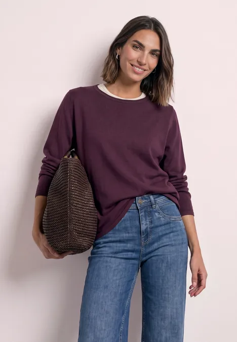 Trui met ronde hals en omgeslagen randen berry maroon Vrouw in paarse trui en spijkerbroek, met grote tas, glimlachend voor een lichte muur.