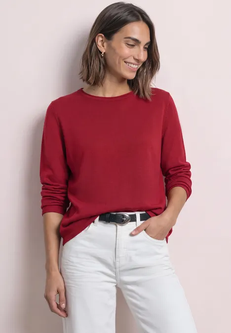 Trui met ronde hals en omgeslagen randen inferno red Vrouw in rode trui met lange mouwen en witte jeans, glimlachend met één hand in de zak.