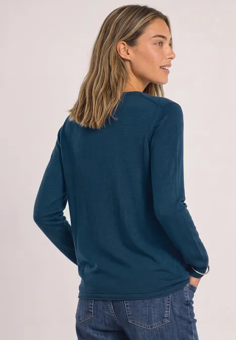 Frau von hinten in lässigem dunkelgrünem Langarmshirt und Jeans, eine Hand in der Hosentasche.