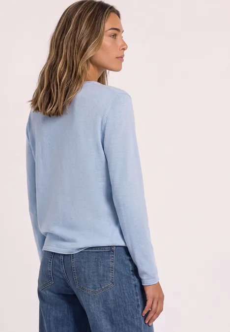 Trui met ronde hals en omgeslagen randen pale blue mel. Vrouw in lichtblauwe trui en spijkerbroek, zijaanzicht tegen neutrale achtergrond.