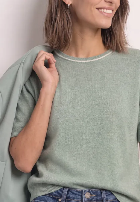 Frau im hellgrünen Pullover, hält eine zum Outfit passende Jacke lässig über die Schulter.