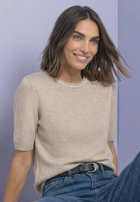 Kurzarm Pullover mit Kontrastdetail clay sand mel. Eine lächelnde Frau mit kurzem braunem Haar, beigem Kurzarm-Pullover und blauer Jeans vor lila Hintergrund.