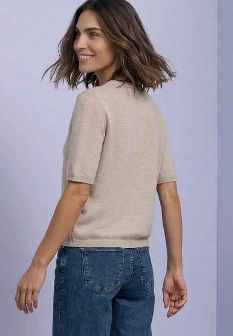 Kurzarm Pullover mit Kontrastdetail clay sand mel. Frau in beigem Kurzarmpulli und blauen Jeans schaut lächelnd über die Schulter vor hellem Hintergrund.