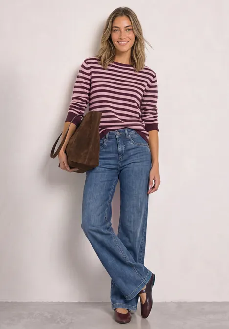 Pullover mit Boat Neck und Streifen rustic rouge mel. Frau im gestreiften Pullover, weiten Jeans und braunen Loafers trägt eine braune Tasche und lächelt.