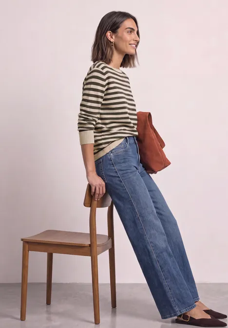 Pullover mit Boat Neck und Streifen clay sand mel. Frau in gestreiftem Pullover und weitem Jeans lehnt an Stuhl und hält eine braune Tasche.