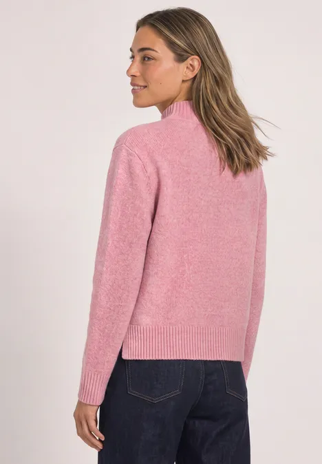 Femme en pull rose et jean bleu, vue de dos, légèrement de profil.