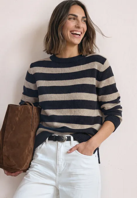 Pullover mit Boat Neck und Streifen indigo night Eine lächelnde Frau in gestreiftem Pullover, weißer Hose und brauner Tasche vor hellem Hintergrund.