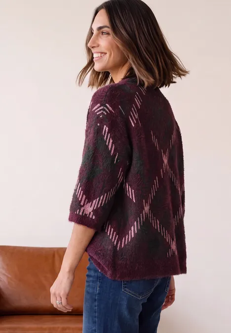 Vrouw in profiel met bordeauxrode gebreide vest met geometrisch patroon en jeans.