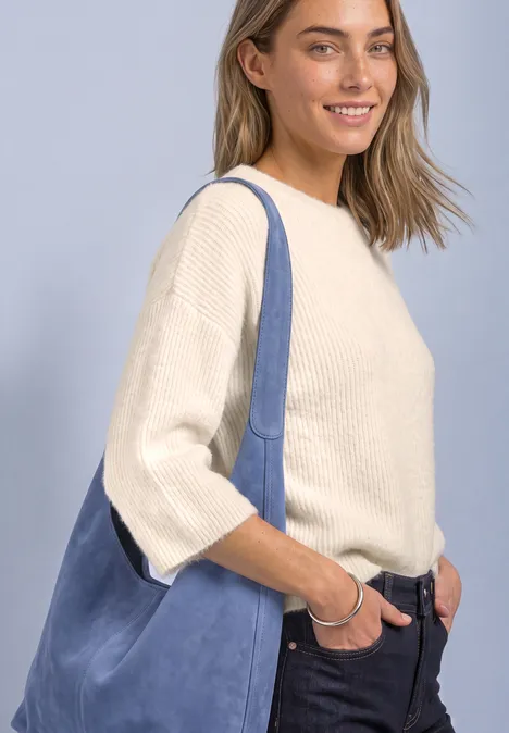Jeune femme souriante en pull crème, jean et grand sac à bandoulière bleu.