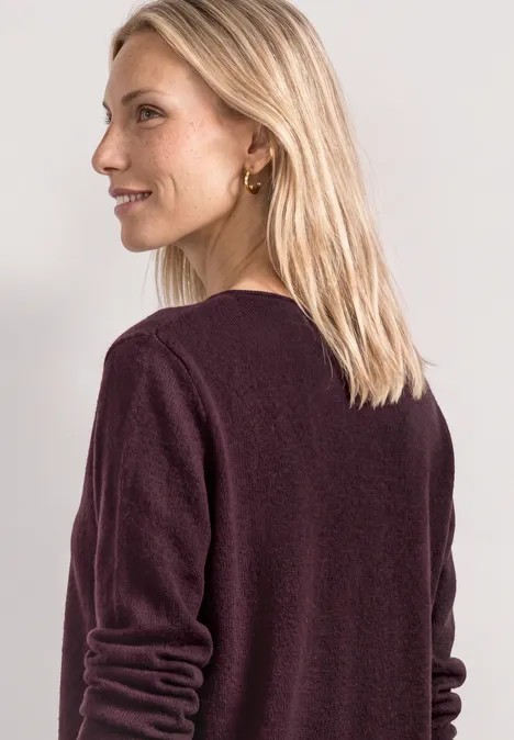 Een vrouw met blond haar draagt een bordeauxrode trui en kijkt opzij.