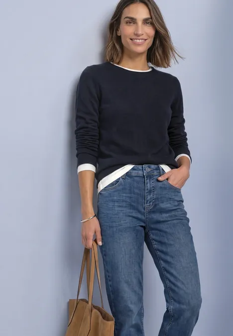 Frau in schwarzem Pullover und Jeans trägt eine Handtasche