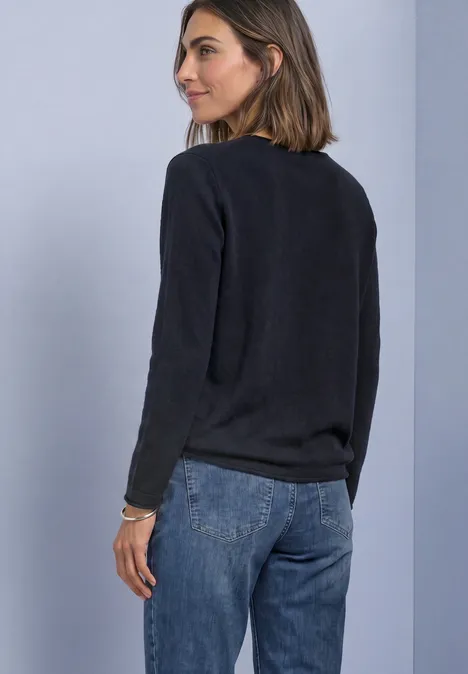 Eine Frau in einem schwarzen Pullover und Jeans blickt über die Schulter nach rechts.