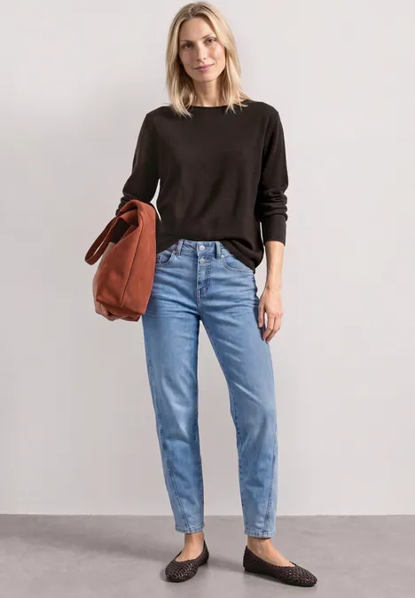 Vrouw in zwarte trui, lichtblauwe jeans en zwarte ballerina's met een roestkleurige tas.