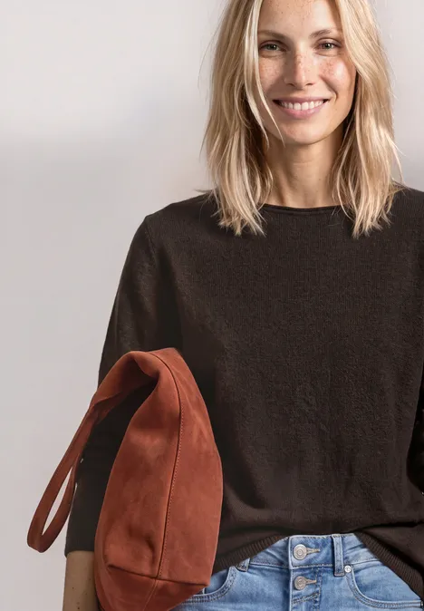 Lachende blonde vrouw in donkerbruin truitje met een roestkleurige tas