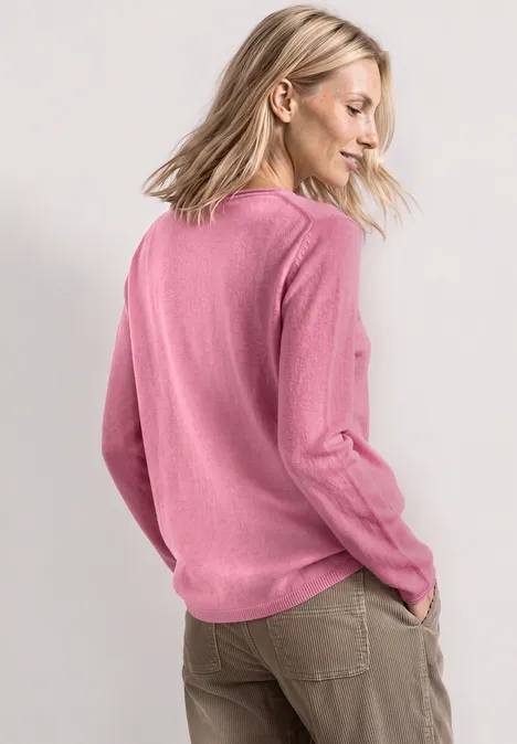 Frau mit blonden Haaren in pinkem Pullover und olivgrüner Hose, seitlich von hinten fotografiert.