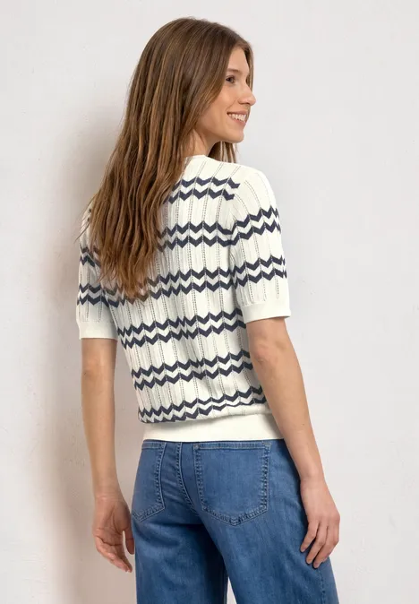 Vue de dos d’une personne en jean bleu et t-shirt blanc à rayures zigzag bleu foncé sur fond clair.