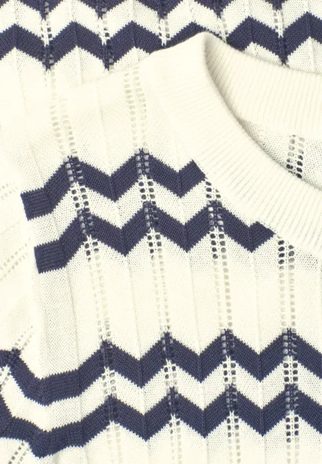 Gros plan d'un pull blanc en tricot avec des rayures en zigzag bleu marine.