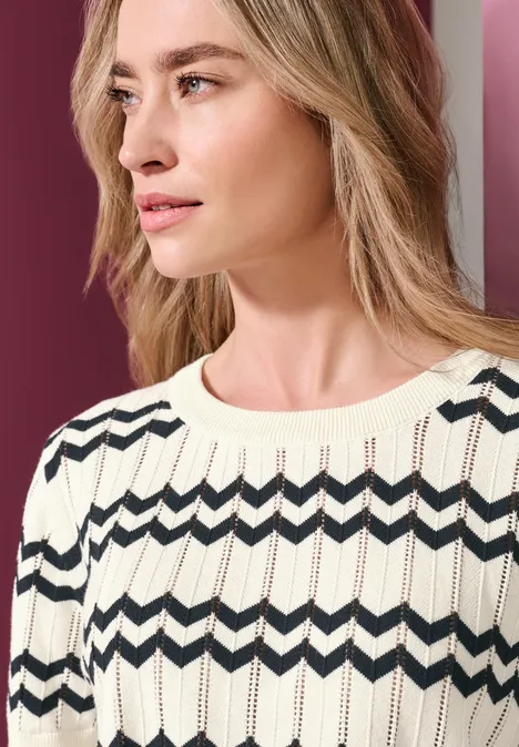 Femme portant un pull tricoté clair à motif zigzag foncé, regard de profil vers la droite.