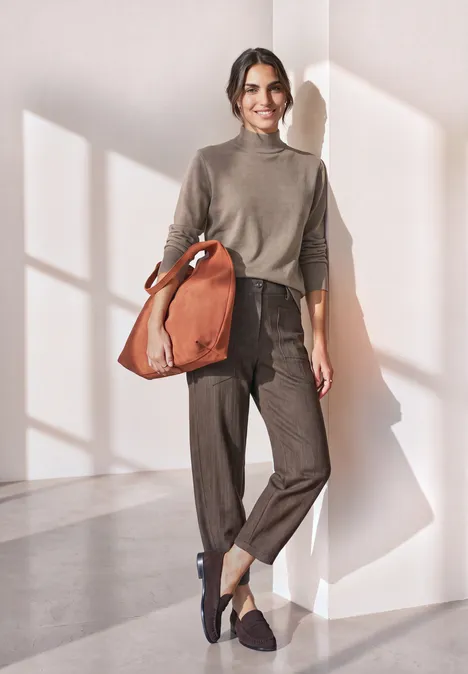 Basic Pullover mit Turtle Neck sanded amber mel. Eine junge Frau in lässigem Outfit und brauner Tasche steht in hellem Raum.