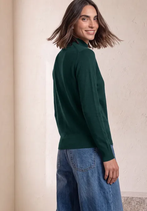 Basic Pullover mit Turtle Neck shadow teal Eine Frau in dunkelgrünem Pullover und blauen Jeans blickt über die Schulter und lächelt.