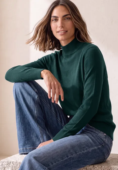 Basic Pullover mit Turtle Neck shadow teal Frau sitzt lächelnd in Jeans und grünem Rollkragenpullover.