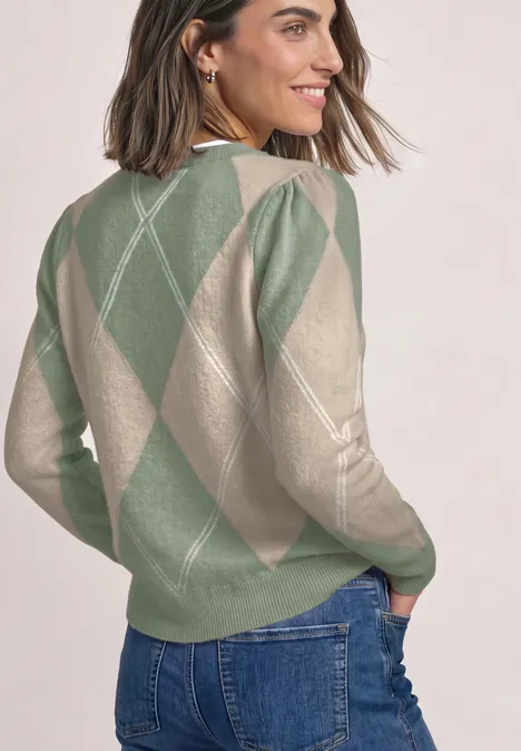 Frau im grün-beige karierten Argyle-Pullover, schaut lächelnd über die Schulter.