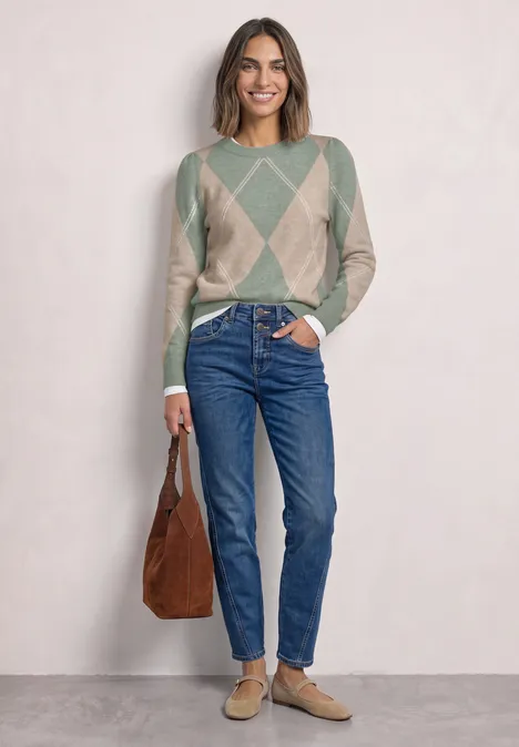 Frau in argyle-grau-beigem Pullover, blauen Jeans, beigen Loafers und brauner Tasche.