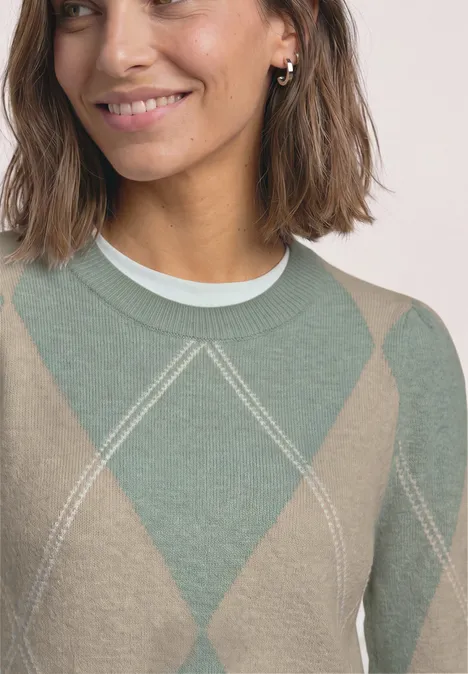 Frau mit diagonalmusterigem Pullover in Grün und Beige, lächelt leicht