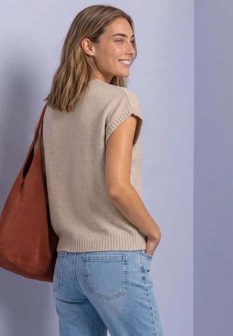 Mouwloze trui met ronde hals light sepia sand Junge Frau in beigem Stricktop, Jeans und brauner Tasche schaut lächelnd über die Schulter.