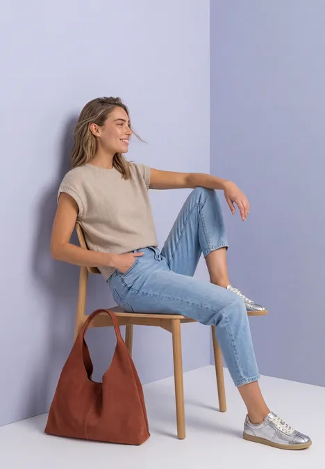 Mouwloze trui met ronde hals light sepia sand Eine Frau sitzt entspannt auf einem Stuhl, trägt Jeans, beiges Top und silberne Sneaker, Tasche am Boden.