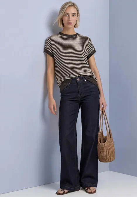 Ärmelloser Pullover mit Rundhals black coffee Frau in gestreiftem T-Shirt, weiten Jeans und Strohtasche vor hellgrauer Wand.